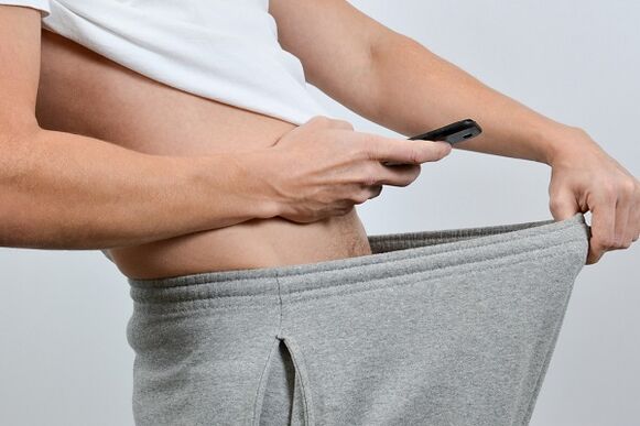 a man looks down his trousers at his engorged penis